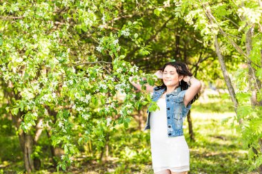 Yeşil parkta yürüyen yaz elbiseli kadın güneşin tadını çıkarıyor. Güneşli bir günde neşeli ve güzel melez bir yarış kızı.