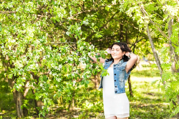 Mujer de primavera en vestido de verano caminando en el parque verde disfrutando del sol. Chica juguetona y hermosa raza mixta en un día cálido y soleado —  Fotos de Stock