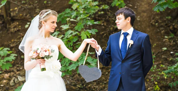 Bride and groom holding a heart shaped  sign. — Stock Photo, Image