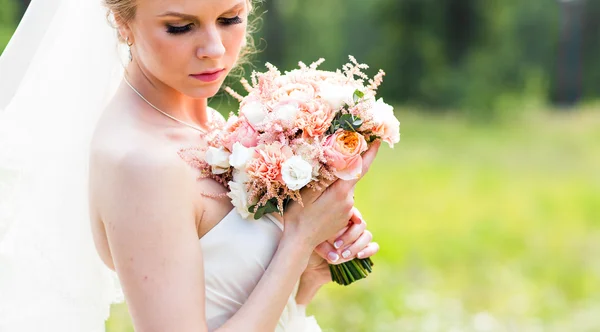 Mooie bruid met bruiloft boeket van bloemen buitenshuis in groen park. — Stockfoto