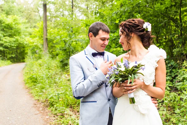 Φύση την άνοιξη νύφη και το γαμπρό στο περπάτημα σε εξωτερικούς χώρους για την ημέρα του γάμου. Ευτυχισμένος νεόνυμφο αγκαλιάζοντας σε καταπράσινο πάρκο. — Φωτογραφία Αρχείου