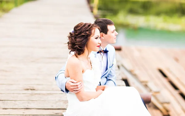 Hermosa joven pareja de boda sentada en el muelle —  Fotos de Stock