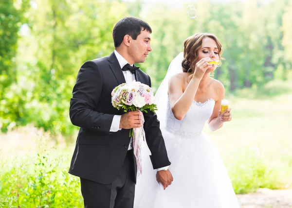 Элегантный стильный жених и счастливая великолепная невеста весело провести время с пузырьком воздуходувка на открытом воздухе в парке — стоковое фото