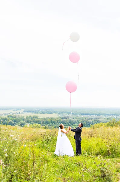Vőlegény és menyasszony léggömbökkel a zöld mező — Stock Fotó