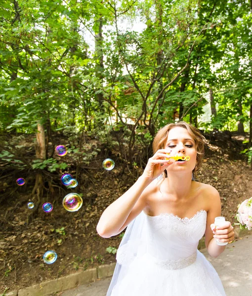 Щаслива розкішна наречена розважається з бульбашками на відкритому повітрі в парку — стокове фото