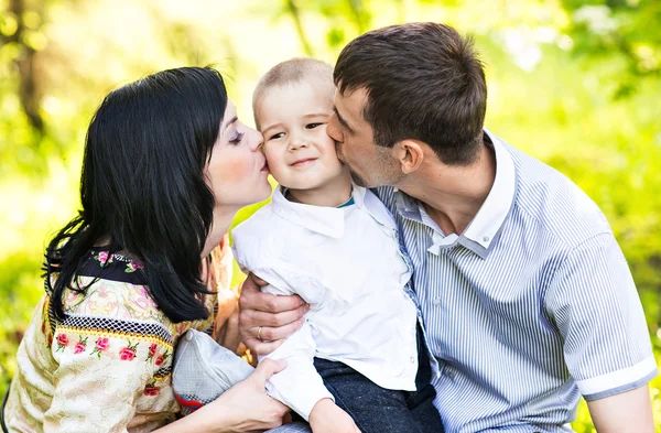 Glückliche Mutter und Vater küssen ihren kleinen Sohn im Park — Stockfoto