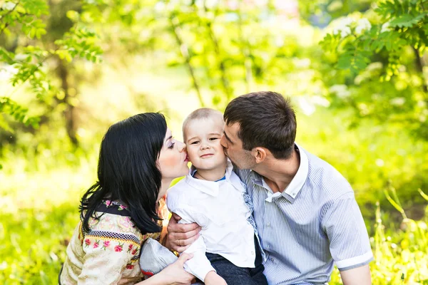 Glückliche Mutter und Vater küssen ihren kleinen Sohn im Park — Stockfoto