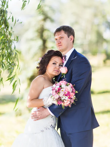 Pareja de boda abrazándose, la novia sosteniendo un ramo de flores, novio abrazándola —  Fotos de Stock