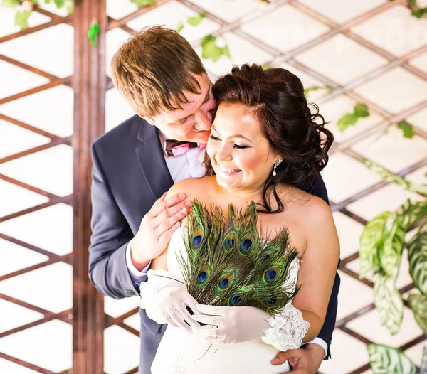 Hochzeitspaar umarmt, Braut hält Pfauenfedern in der Hand, der Bräutigam umarmt sie — Stockfoto