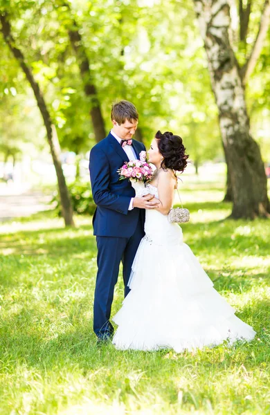 Pareja de boda abrazándose, la novia sosteniendo un ramo de flores, novio abrazándola —  Fotos de Stock