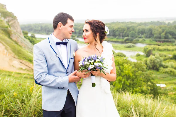 Noiva e noivo no dia do casamento andando ao ar livre na natureza de primavera. Feliz recém-casado abraçando no parque verde . — Fotografia de Stock