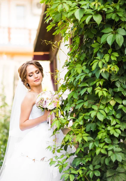 Vackra brud flicka i bröllopsklänning och bukett blommor, utomhus porträtt — Stockfoto