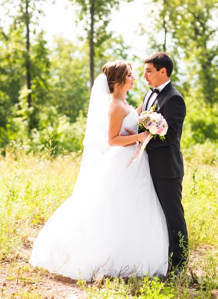 O noivo e a noiva num parque. Buquê de casamento nupcial de flores — Fotografia de Stock