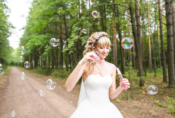 Hermosa mujer joven con vestido de novia blanco soplando burbuja al aire libre —  Fotos de Stock