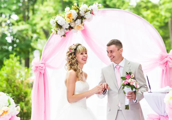 Happy bride putting a ring on grooms finger during wedding ceremony