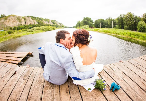 Mooie jonge bruidspaar zittend op de pier — Stockfoto