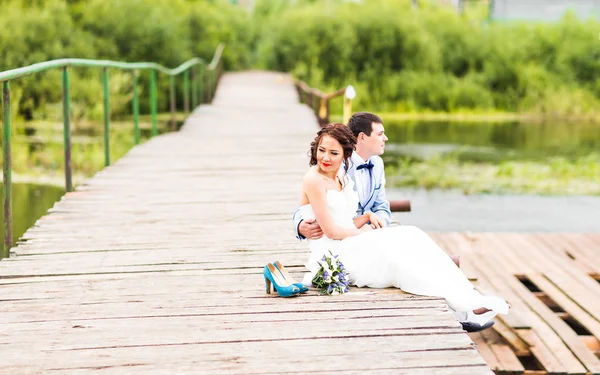 Mooie jonge bruidspaar zittend op de pier — Stockfoto