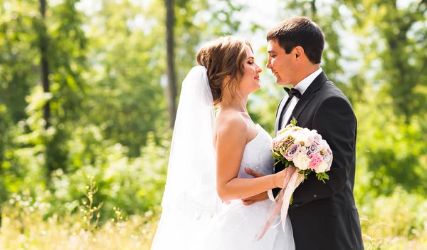 O noivo e a noiva num parque. Buquê de casamento nupcial de flores — Fotografia de Stock