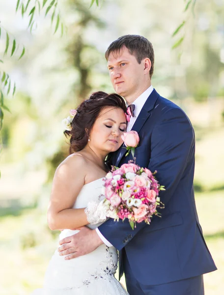 Couple de mariage câlin, la mariée tenant un bouquet de fleurs, marié embrassant son — Photo