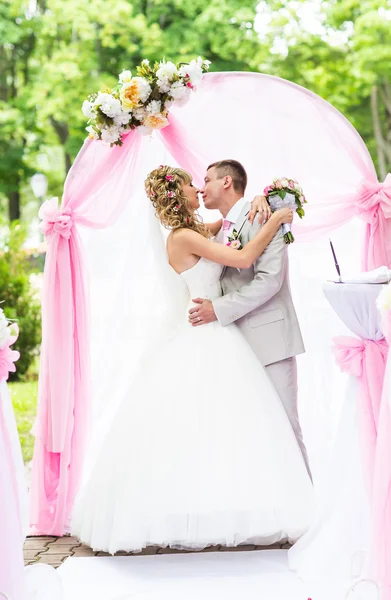 Feliz casal romântico recém-casado beijando no corredor do casamento com decorações e flores rosa — Fotografia de Stock