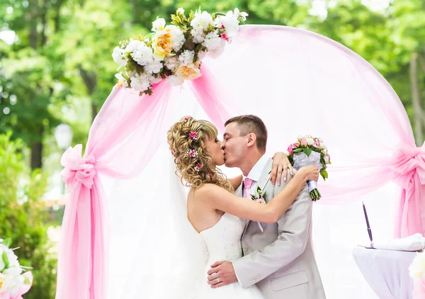 Felice coppia romantica appena sposata baciare alla navata nuziale con decorazioni rosa e fiori — Foto Stock