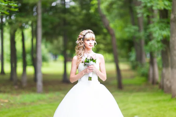 Красивая невеста со свадебным букетом цветов на открытом воздухе в зеленом парке . — стоковое фото