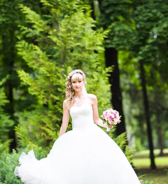 Mooie bruid met bruiloft boeket van bloemen buitenshuis in groen park. — Stockfoto