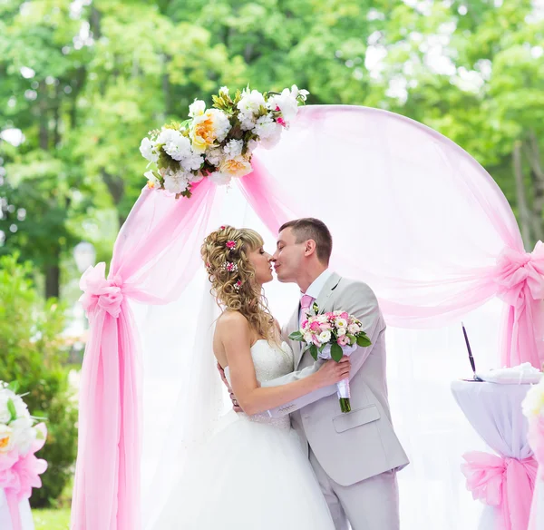 Feliz casal romântico recém-casado beijando no corredor do casamento com decorações e flores rosa — Fotografia de Stock