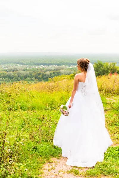 Vackra brud flicka i bröllopsklänning och bukett blommor, utomhus porträtt — Stockfoto