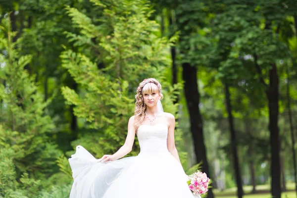 Vackra brud med bröllop bukett blommor utomhus i grön park. — Stockfoto