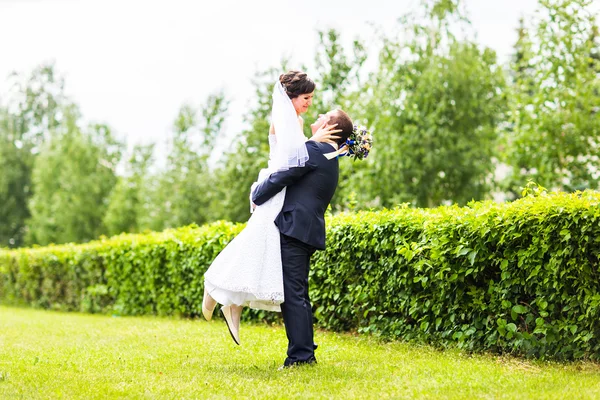 Feliz noivo segurando jovem noiva bonita em seus braços — Fotografia de Stock