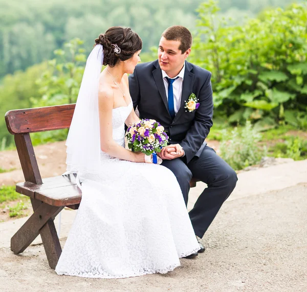 Aantrekkelijke bruid en bruidegom zittend op een bankje — Stockfoto