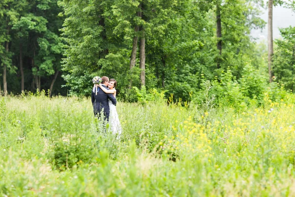 Pareja de boda abrazándose, la novia sosteniendo un ramo de flores, novio abrazándola —  Fotos de Stock