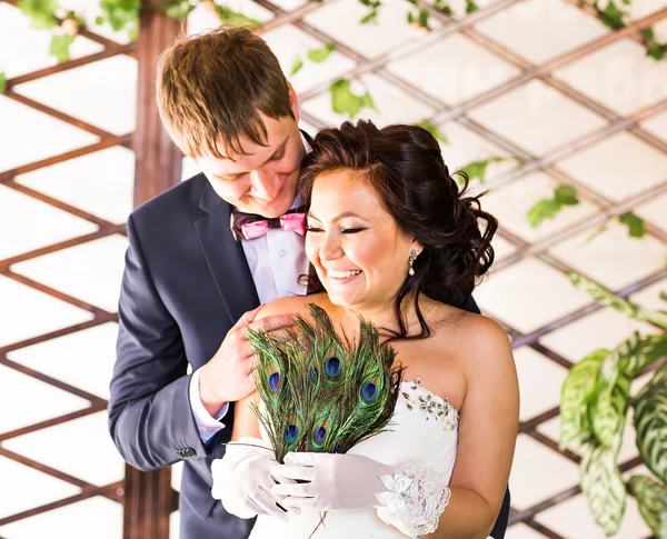 Hochzeitspaar umarmt, Braut hält Pfauenfedern in der Hand, der Bräutigam umarmt sie — Stockfoto