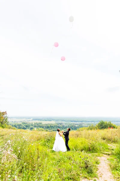 Жених и невеста с воздушными шарами на зеленом поле — стоковое фото