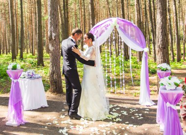 Harika şık zengin mutlu gelin ve damat yeşil bahçe çiçekli mor arch yakınındaki bir düğün töreninde dans