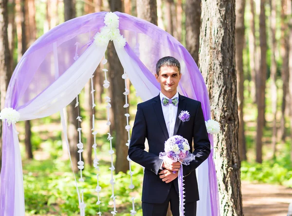 Ricco sposo elegante con bouquet da sposa in attesa sposa vicino all'arco di nozze — Foto Stock