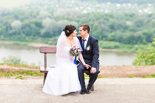 Aantrekkelijke bruid en bruidegom zittend op een bankje — Stockfoto