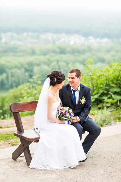 Aantrekkelijke bruid en bruidegom zittend op een bankje — Stockfoto