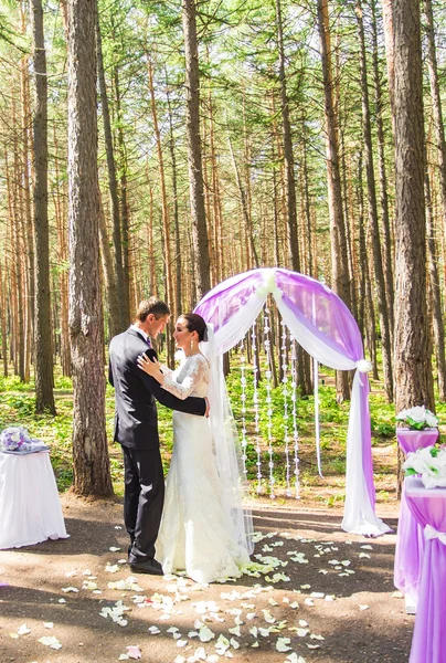 Maravilloso elegante novia feliz y novio bailando en una ceremonia de boda en el jardín verde cerca del arco púrpura con flores —  Fotos de Stock