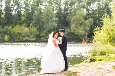 Düğün çift ayakta ve göl kenarında sarılma.