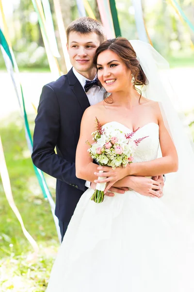 Pareja de boda abrazándose, novia sosteniendo un ramo de flores, el novio abrazándola —  Fotos de Stock