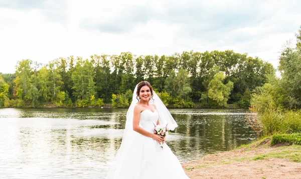 Sposa in abito bianco con bouquet da sposa al lago — Foto Stock