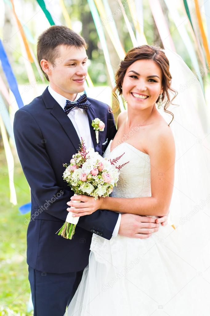 wedding couple kissing,  bride holding a bouquet of flowers, groom embracing her