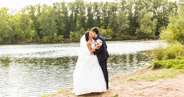 Couple de mariage debout et baisers près du lac . — Photo