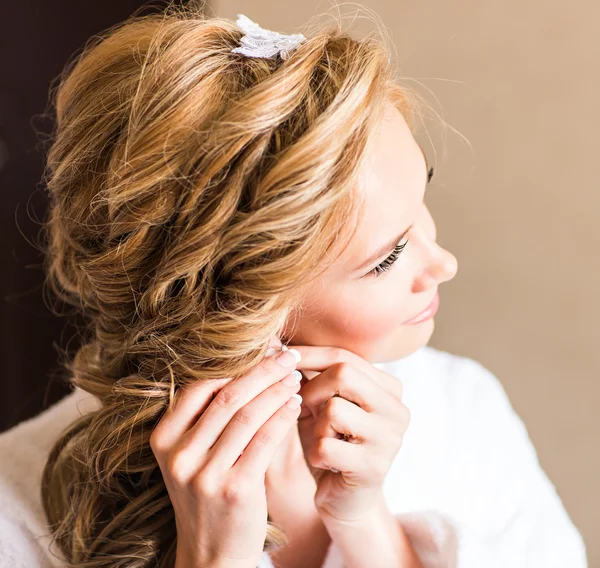 Elegante novia rubia poniéndose los pendientes de cerca, preparándose para la boda —  Fotos de Stock