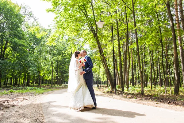 Casal em traje de casamento com buquê de flores ao ar livre, noiva e noivo — Fotografia de Stock