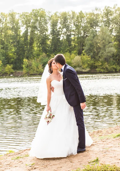 Bruiloft paar staande en kussen in de buurt van lake. — Stockfoto