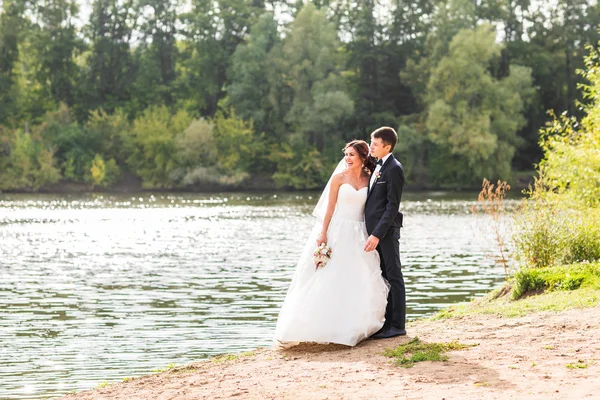 Casamento casal de pé e abraçando perto do lago . — Fotografia de Stock