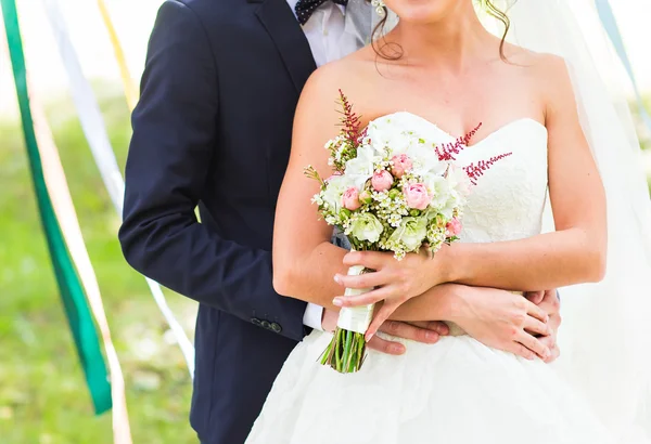 Couple de mariage câlin, mariée tenant un bouquet de fleurs, le marié l'embrassant — Photo